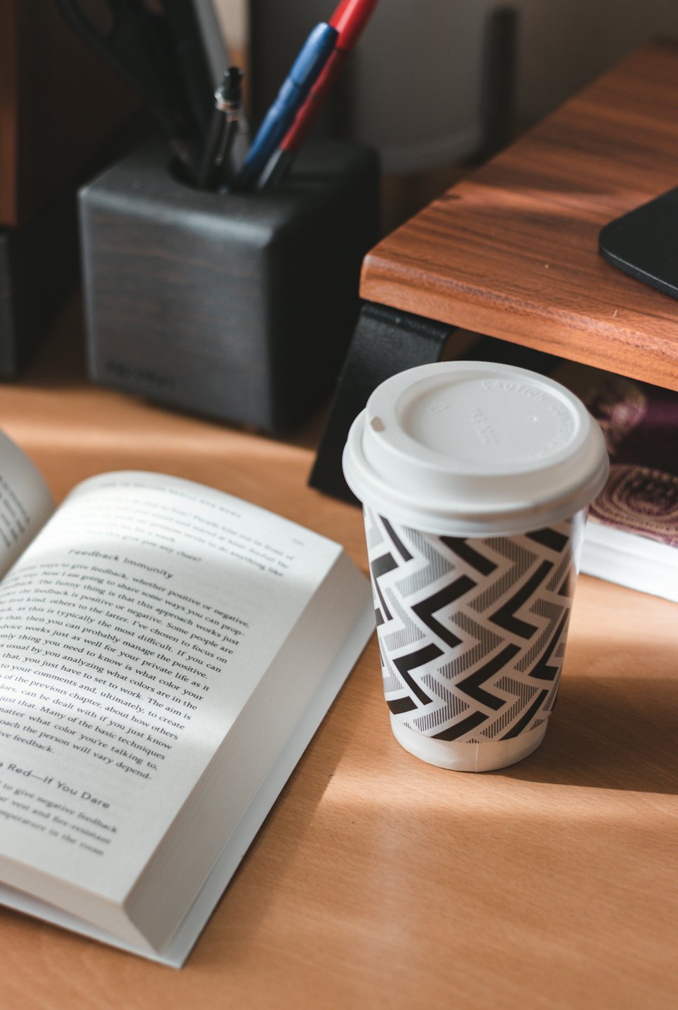 Holzschreibtisch mit offenem Buch und Kaffeetasse.